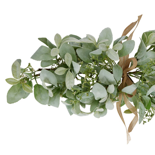 Close view of softly textured pale green oval leaves, fine branching sprays with tiny white details and the looped tan ribbon bow.