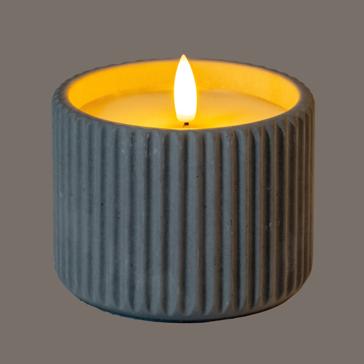 Ribbed LED candle photographed illuminated, with a bright flame-shaped centre, an amber-lit inset top and outer ribs appearing dark grey in the subdued lighting.