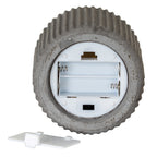 Underside of the ribbed candle showing an open, empty two-channel battery compartment, metal-looking contacts and a black switch, with the white cover beside it.