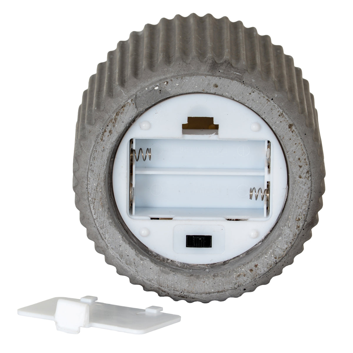 Underside of the ribbed candle showing an open, empty two-channel battery compartment, metal-looking contacts and a black switch, with the white cover beside it.