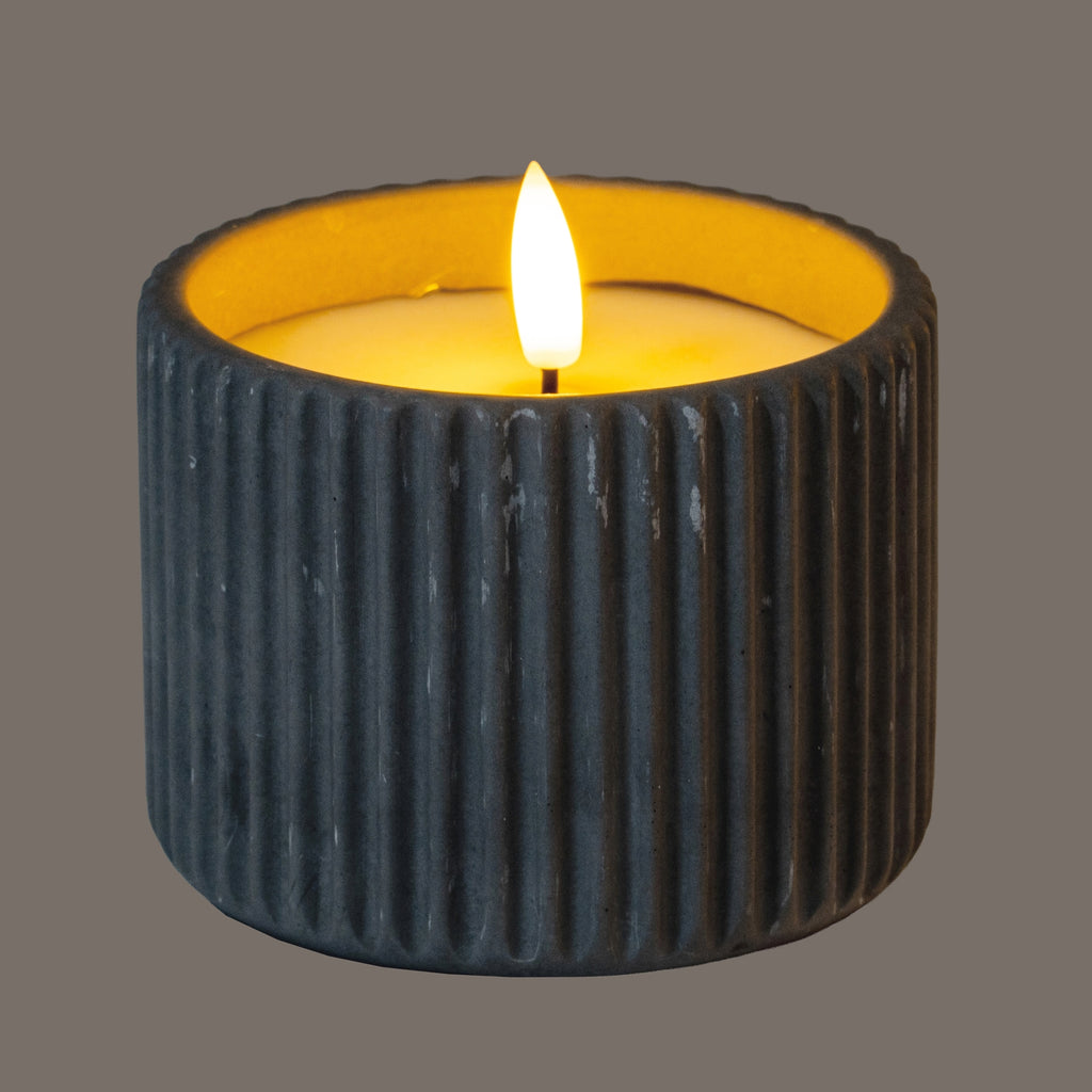 Grey ribbed LED candle shown illuminated, with a yellow glow around the inset top and the outer wall appearing darker in the lighting.