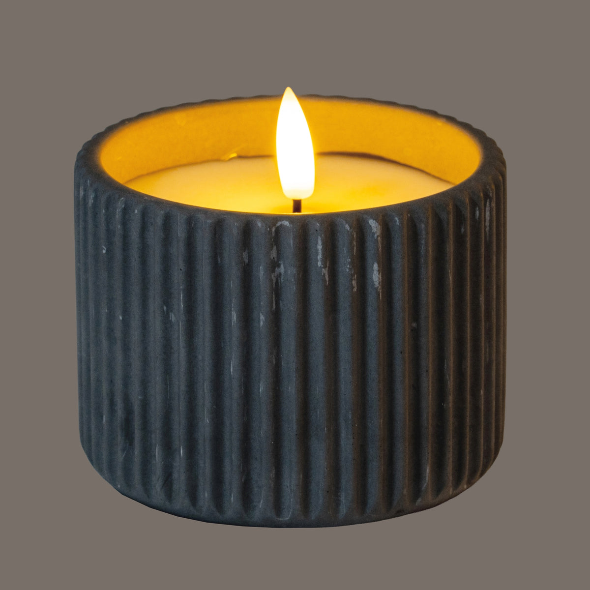 Grey ribbed LED candle shown illuminated, with a yellow glow around the inset top and the outer wall appearing darker in the lighting.