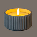 LED candle photographed illuminated, with a bright flame-shaped centre, yellow-lit inset top and ribbed sides appearing dark grey against a grey background.