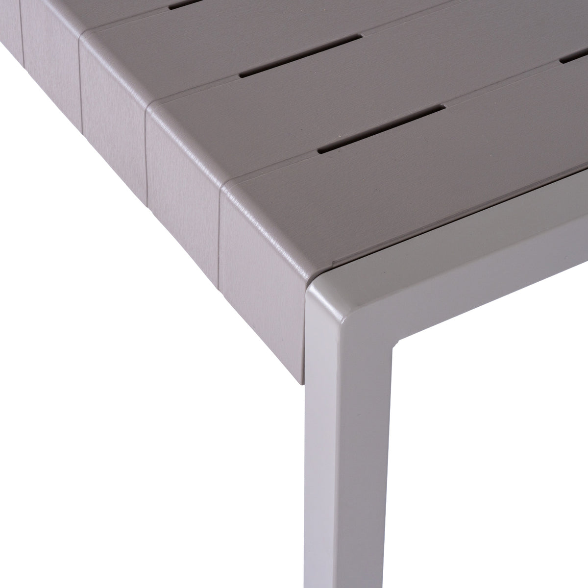 Close-up of the grey tabletop corner showing fine linear texture, staggered narrow slots and the square leg below.