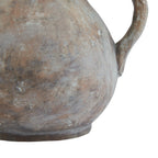 Detail of the jug's rounded lower body and circular foot, with pale streaks across the brown-grey finish and part of the handle at the right.