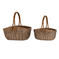 Two empty brown woven trug baskets side by side, with the larger basket on the left and tall arched handles above both oval bodies.