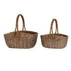 Two empty brown woven trug baskets side by side, with the larger basket on the left and tall arched handles above both oval bodies.