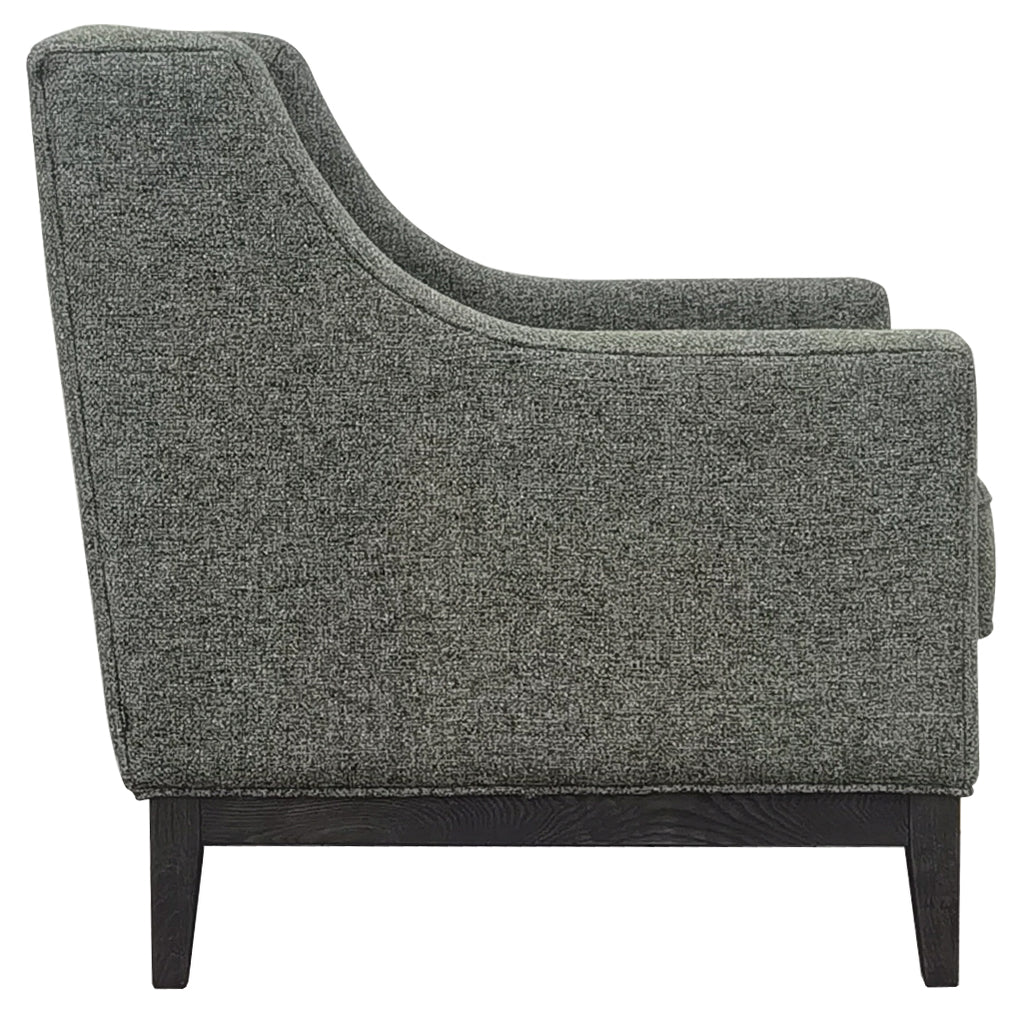 Side view of the green armchair showing its curved arm profile, piped upholstery and dark wooden supporting frame.