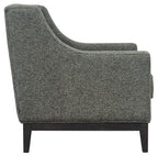 Side view of the green armchair showing its curved arm profile, piped upholstery and dark wooden supporting frame.