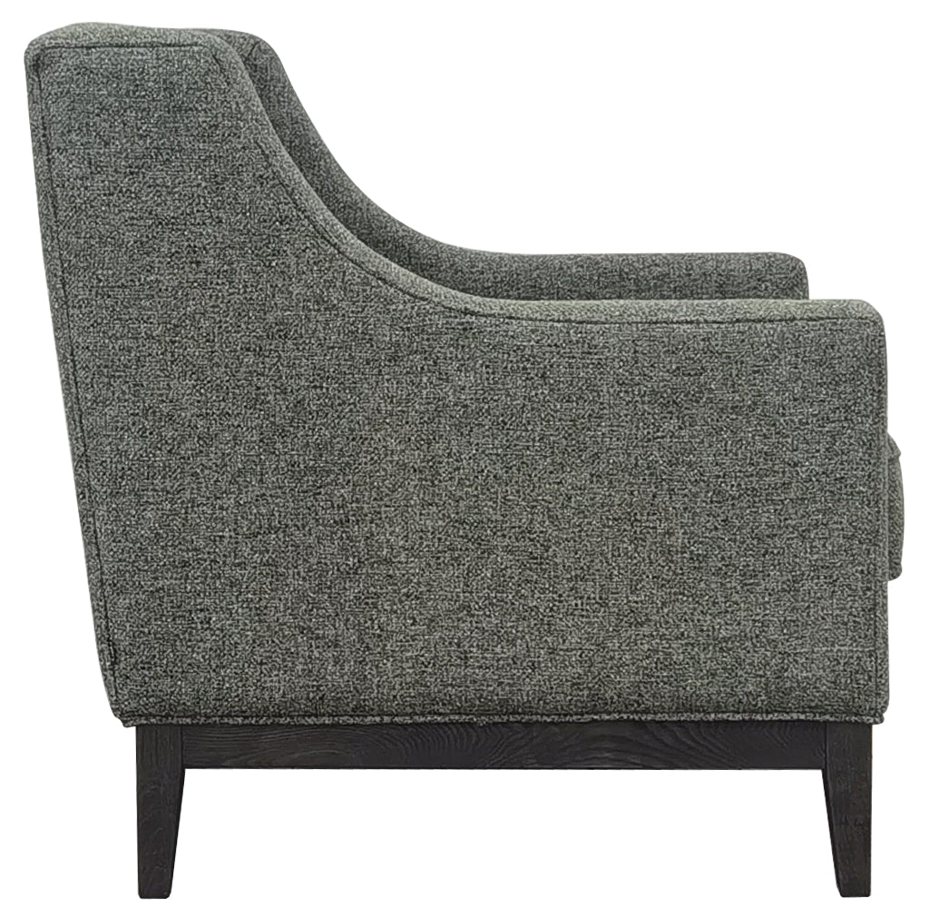 Side view of the green armchair showing its curved arm profile, piped upholstery and dark wooden supporting frame.
