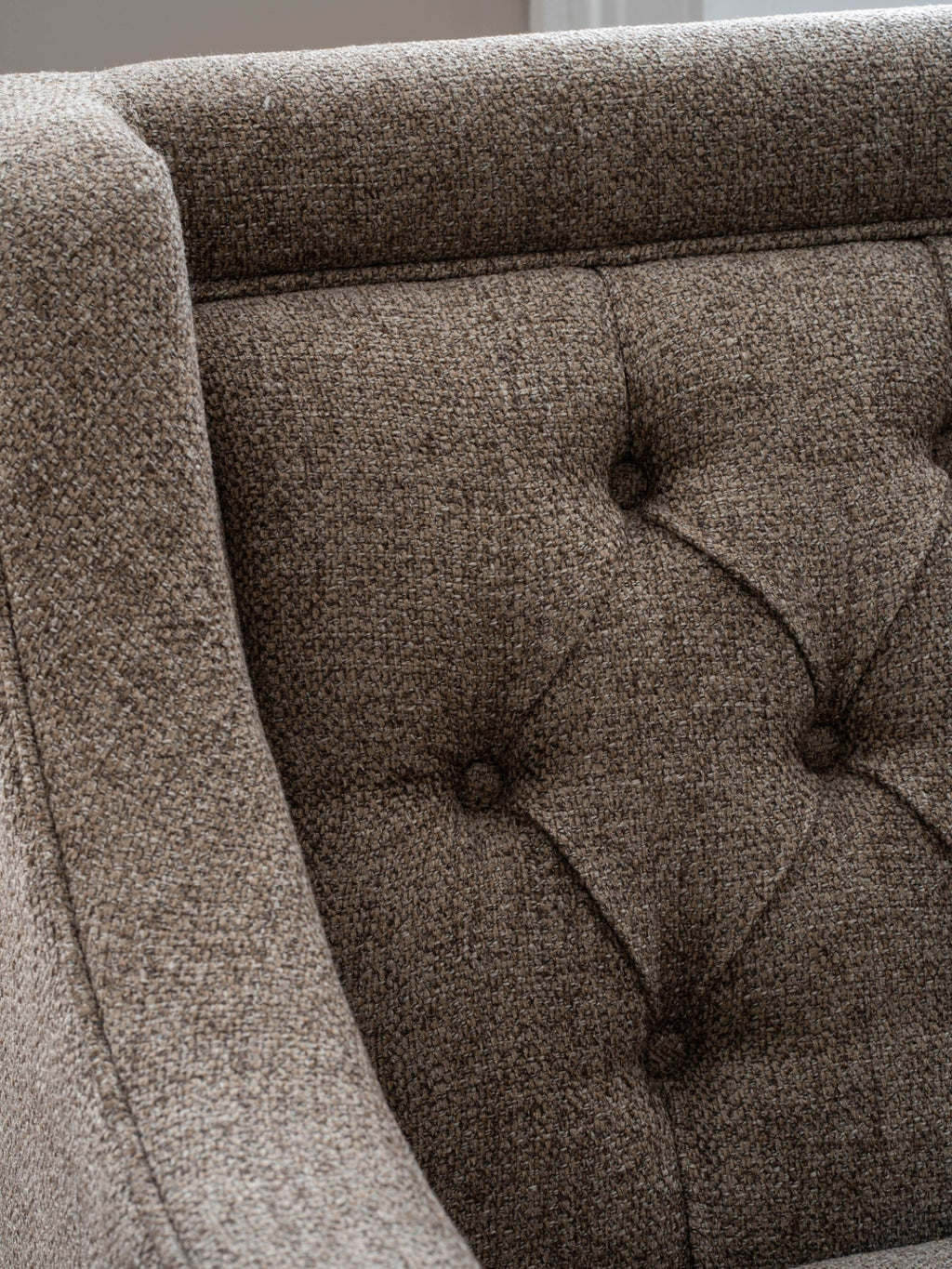 Close-up of the sofa's taupe and beige woven fabric, deep buttoning and piping beside the arm.