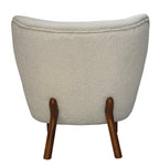 Straight rear view of the cream bouclé chair with a broad curved back, piping along the top and two splayed wooden legs.