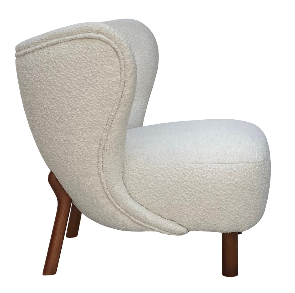 Side view of the cream bouclé chair showing its rounded seat, curved upholstered back, piped outline and brown wooden legs.