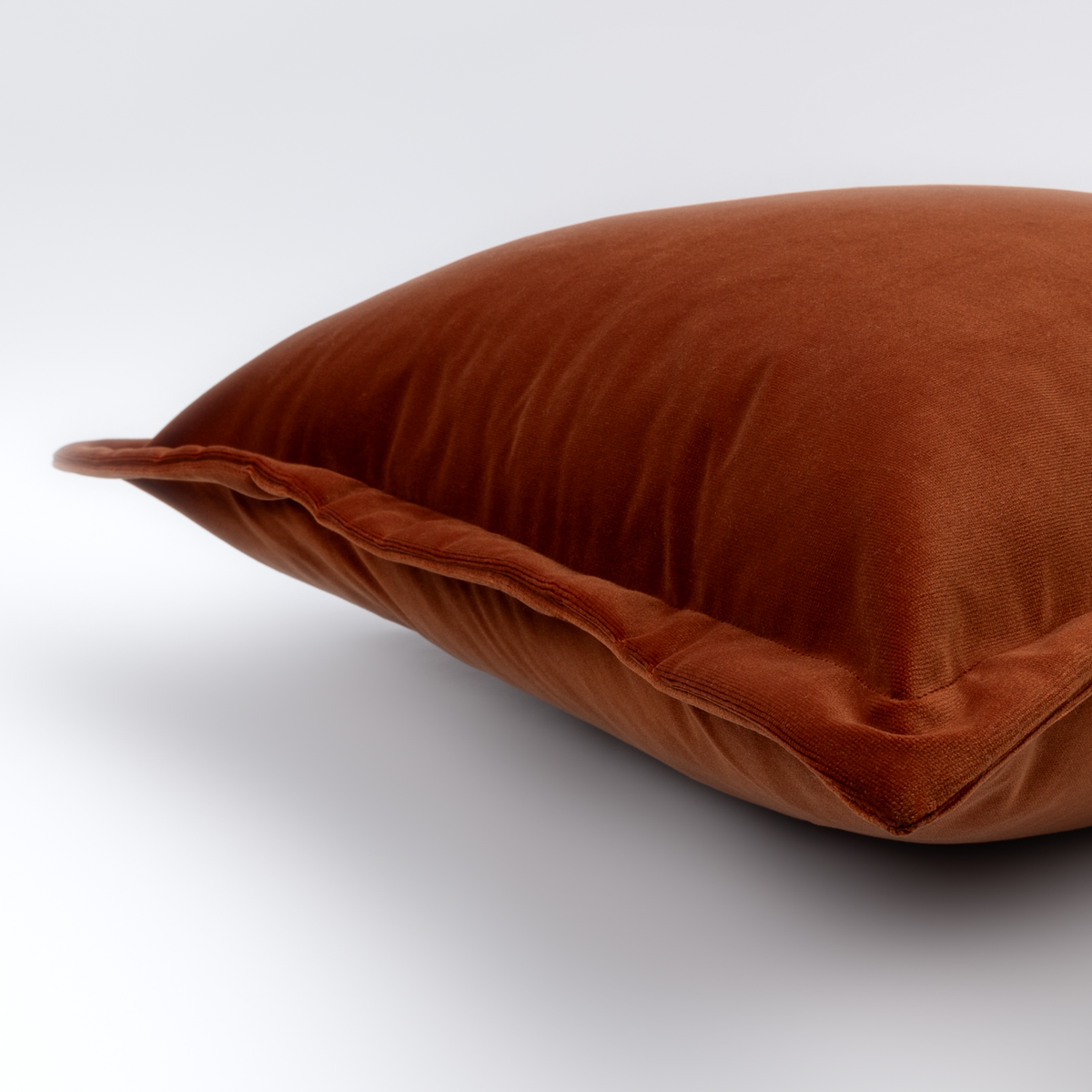 Angled close-up of the rust velvet Caldera Cushion with its piped edge