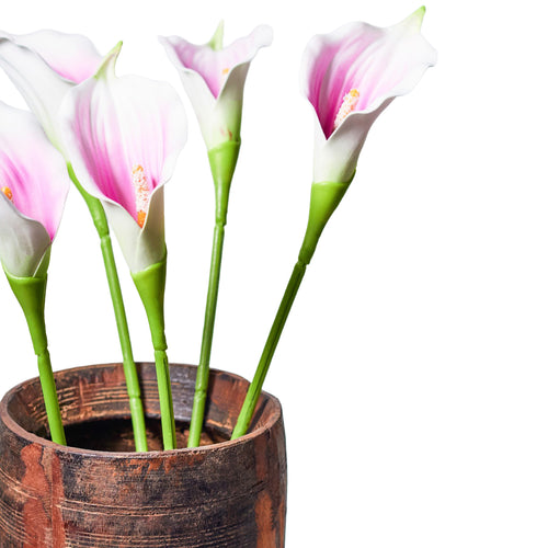 Close-up of cream-white and lilac-pink faux calla lilies on green stems in a brown vessel with visible grain, against a white background.