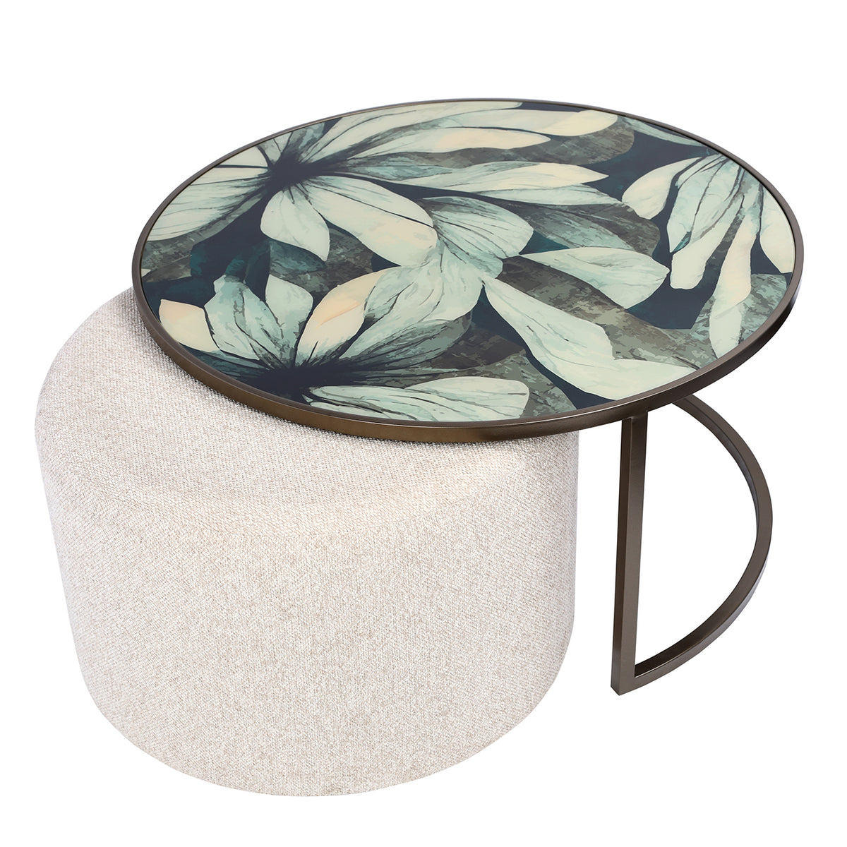 Elevated angled view of the pale leaf-patterned tabletop, with the round oatmeal pouffe extending beneath it to the left.