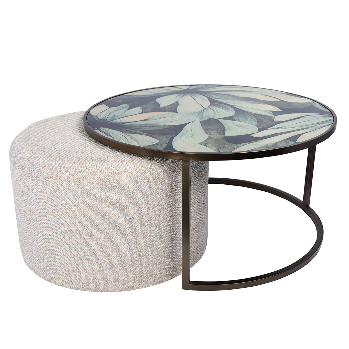Round botanical glass coffee table with an oatmeal pouffe partly pulled out to the left of its open frame.