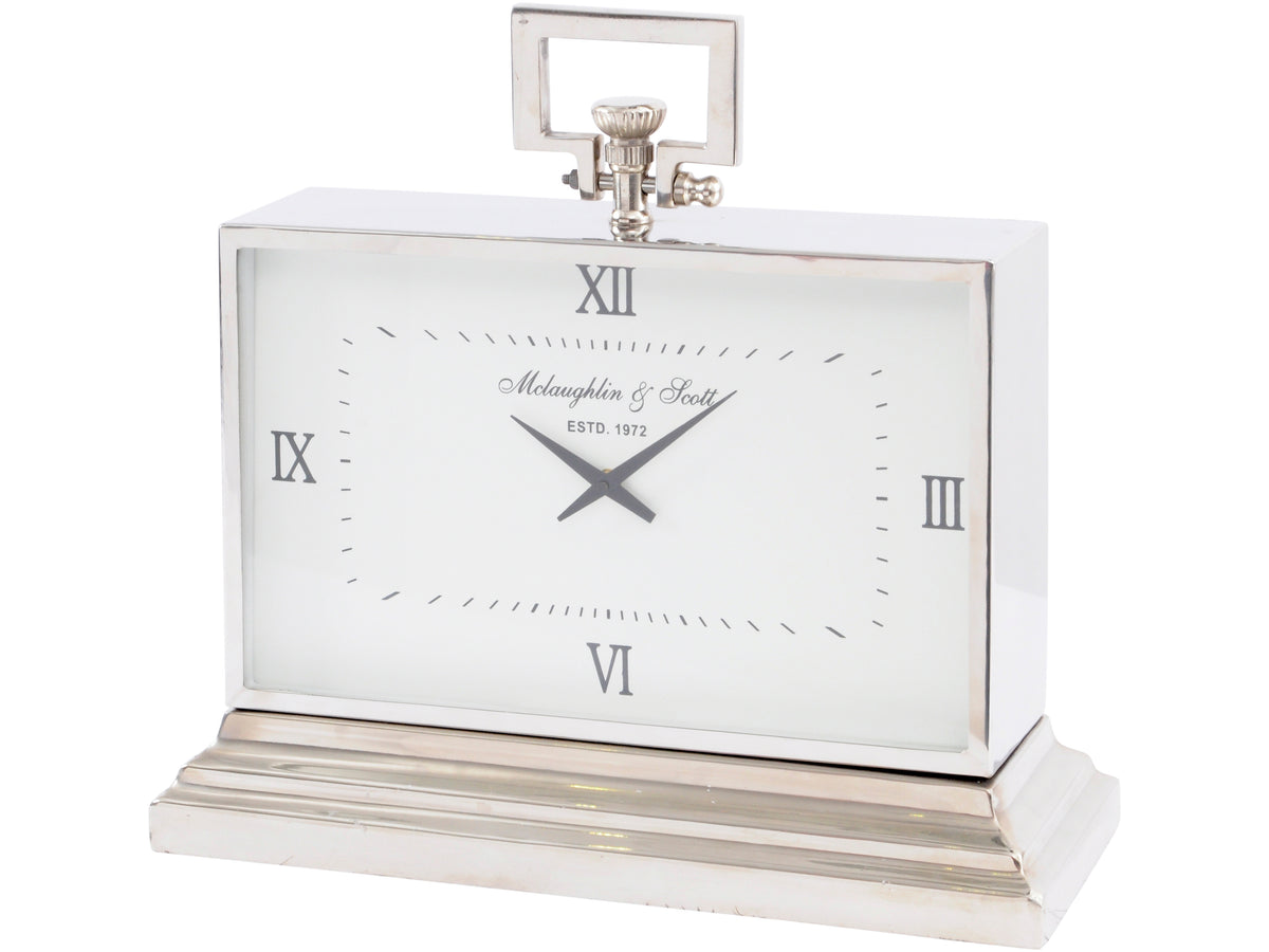 Silver carriage table clock viewed slightly from the right, showing a white Roman numeral dial, stepped plinth and rectangular top loop.