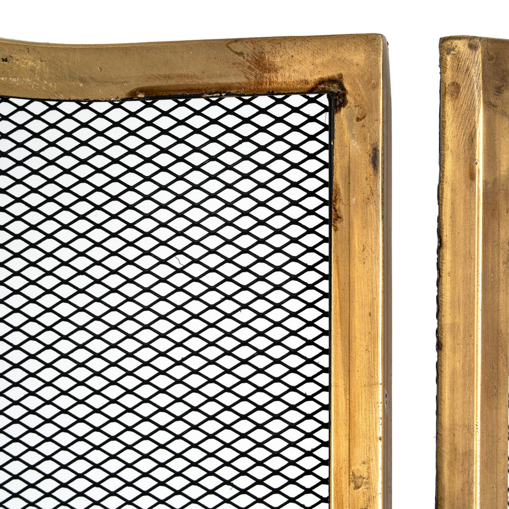 Close-up of black diamond mesh beside the brass-tone panel edges, showing darker markings and surface texture on the frame.