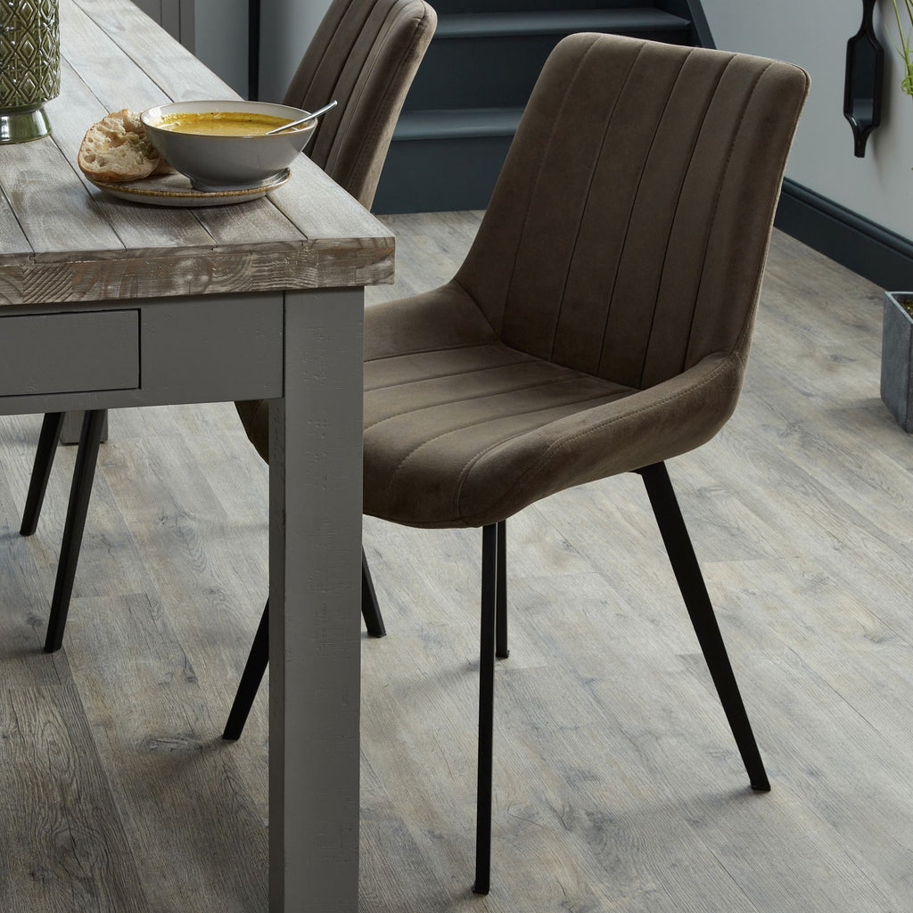 Brown channelled dining chair beside a grey wooden dining table set with soup and bread, with a matching chair behind.