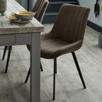 Brown channelled dining chair beside a grey wooden dining table set with soup and bread, with a matching chair behind.
