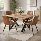Four tan channelled chairs arranged around a timber dining table with black crossed legs, styled with white flowers on a cream rug.