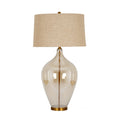 Table lamp against a white background, with a beige tapered shade above a clear bulbous body, visible gold-coloured central stem and circular foot.