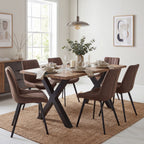 Clear Channel Dining Table styled with brown upholstered chairs, neutral place settings and a vase of foliage beneath a pendant light in a bright dining room.