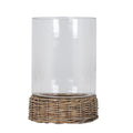 Clear open cylindrical candle lantern rising from a low round brown woven tray, shown empty against a white background.
