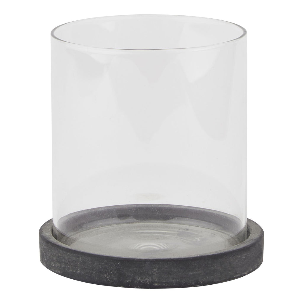 Front view of a clear cylindrical candle lantern on a shallow, mottled dark grey circular base against white.