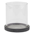 Front view of a clear cylindrical candle lantern on a shallow, mottled dark grey circular base against white.