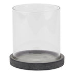 Front view of a clear cylindrical candle lantern on a shallow, mottled dark grey circular base against white.