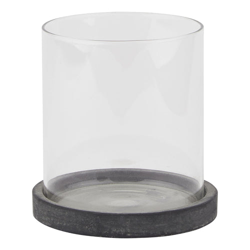 Front view of a clear cylindrical candle lantern on a shallow, mottled dark grey circular base against white.