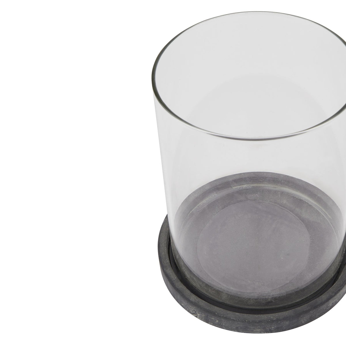 Close angled view of an empty clear cylindrical lantern sleeve seated in a shallow dark grey round base with pale weathered markings, against white.