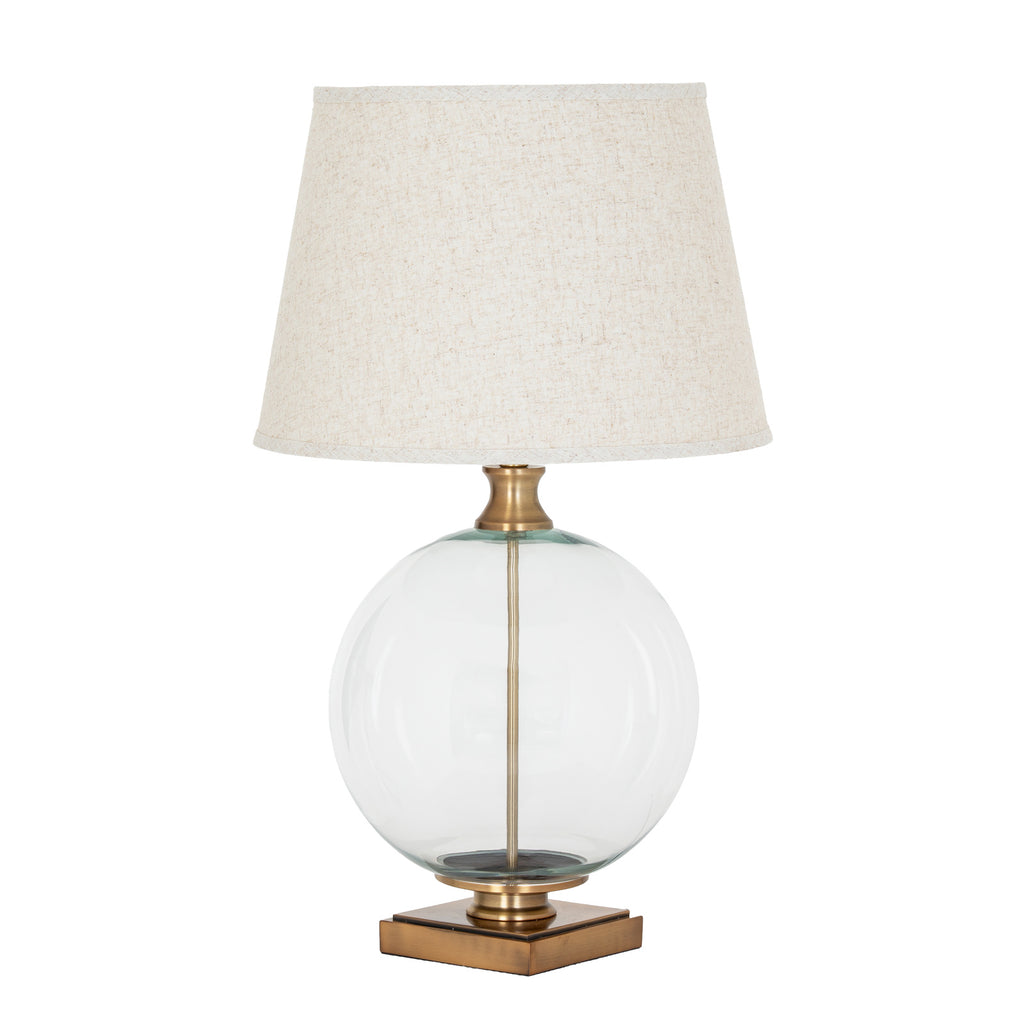 Clear Spherebody Table Lamp on a white background, with a pale tapered shade, transparent round body and brass-toned square base.