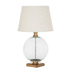 Clear Spherebody Table Lamp on a white background, with a pale tapered shade, transparent round body and brass-toned square base.