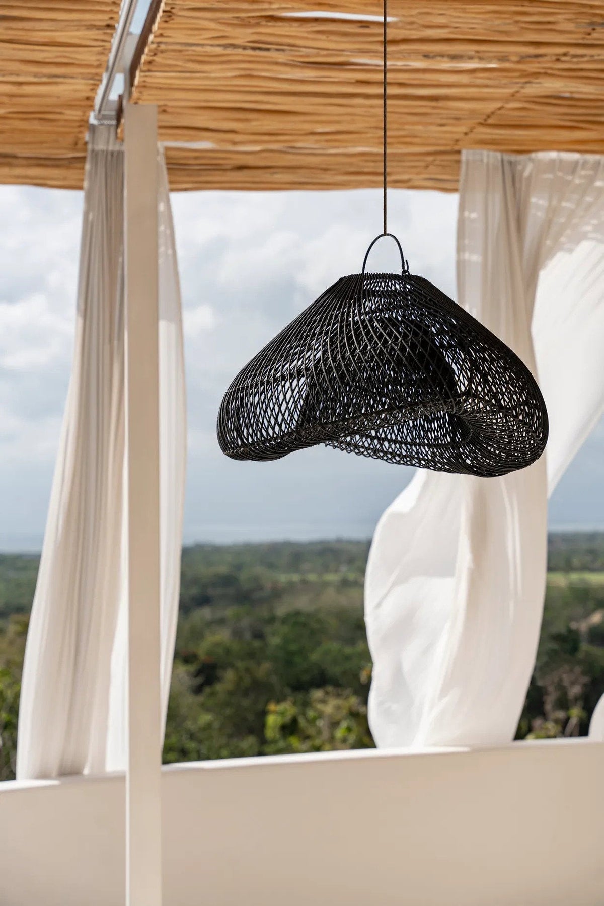 Cloud Rattan Pendant Light – Black, Medium – suspended on an open terrace