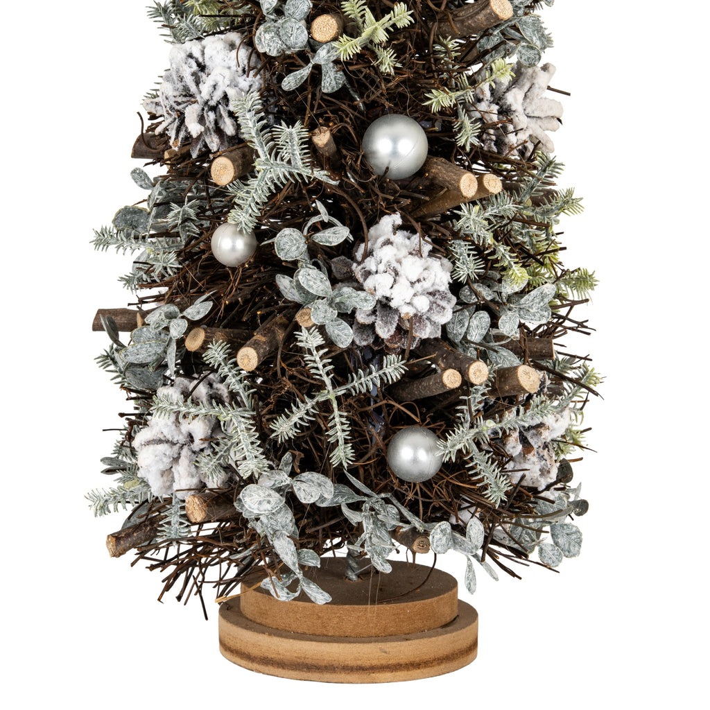 Close-up of the lower tree showing white-frosted pinecones, silver-toned spheres, pale leafy sprigs and cut twig ends above the layered brown base.