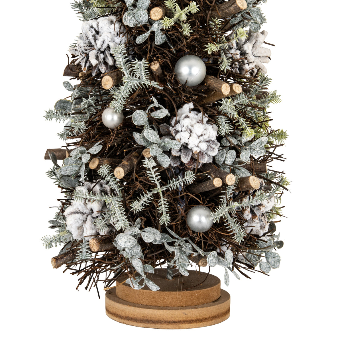 Close-up of the lower tree showing white-frosted pinecones, silver-toned spheres, pale leafy sprigs and cut twig ends above the layered brown base.