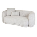 Angled front view of a pale cream curved sofa with a broad seat cushion and square and rectangular cushions arranged at one end.