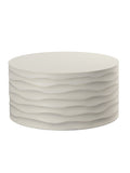 Round cream coffee table viewed from slightly above, with a plain circular top and wavy horizontal ridges edged in brass colour, on a white background.