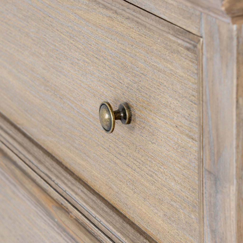 Close-up of a rounded brass-coloured knob against the tan-grey grain-patterned drawer front and its raised border.