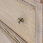 Close-up of a rounded brass-coloured knob against the tan-grey grain-patterned drawer front and its raised border.