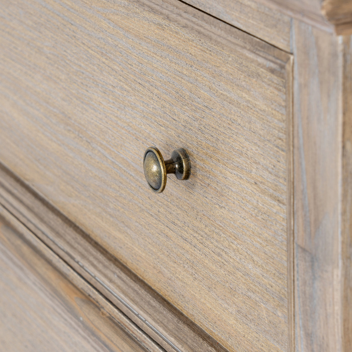 Close-up of a rounded brass-coloured knob against the tan-grey grain-patterned drawer front and its raised border.
