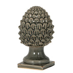 Dark grey acorn ornament with an oval scale-covered crown, flared pedestal and square foot against a white background.