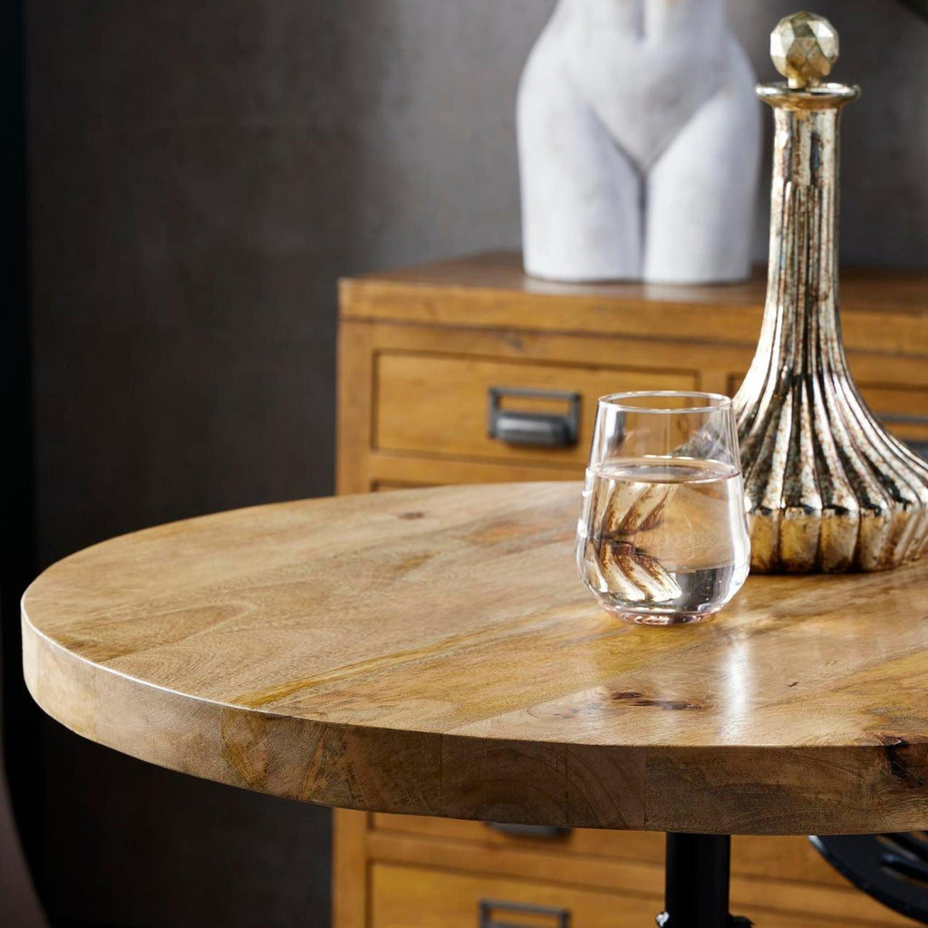 Close view of the round tabletop showing warm grain and its rounded edge, styled with a glass and gold-toned decanter.