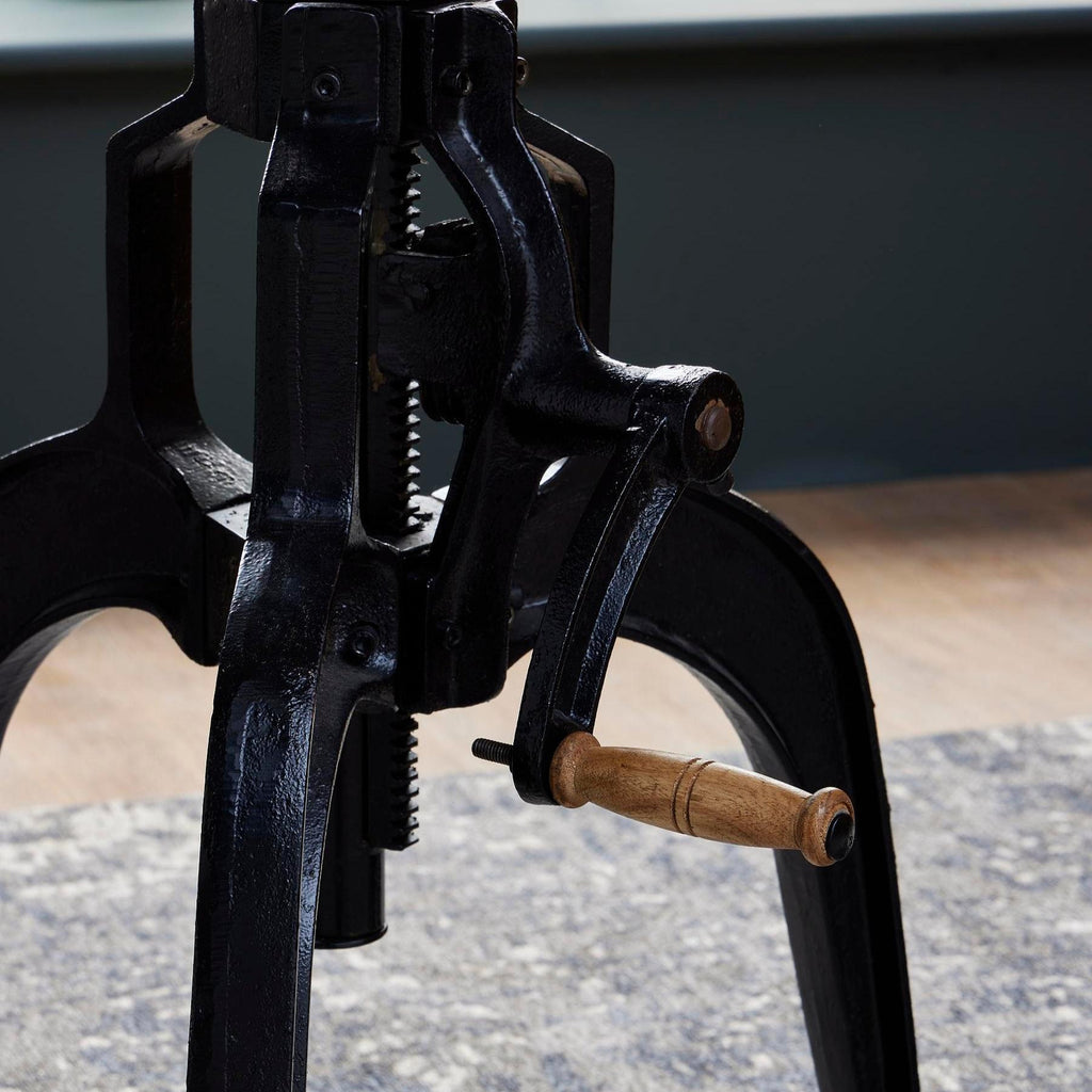 Detail of the textured black table frame, exposed toothed central shaft and crank with a wood-toned handle.