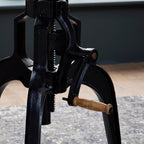 Detail of the textured black table frame, exposed toothed central shaft and crank with a wood-toned handle.