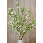 Closer view of cream gypsophila flower clusters branching above the neck of a pale vase, with wood panelling behind.