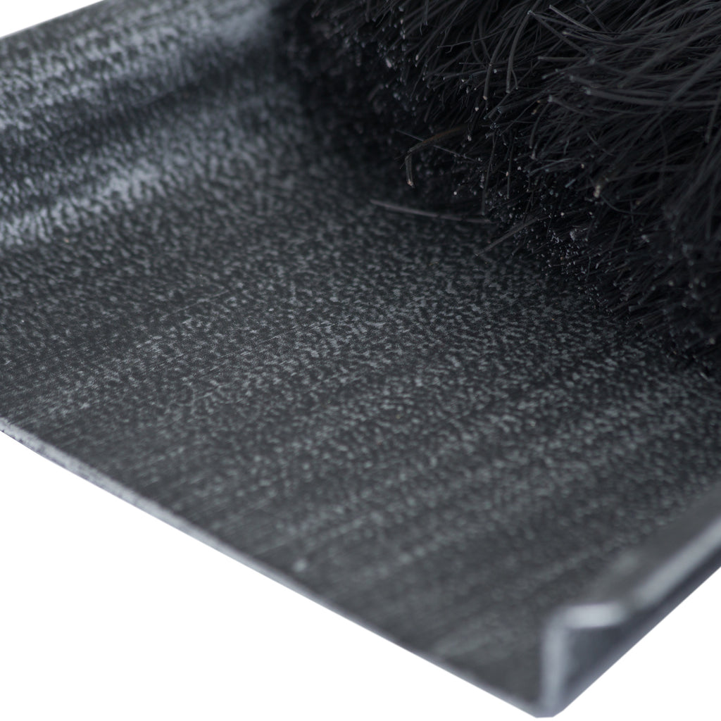 Close-up of the pan’s silver-stippled dark surface and raised edge beside dense black brush bristles.